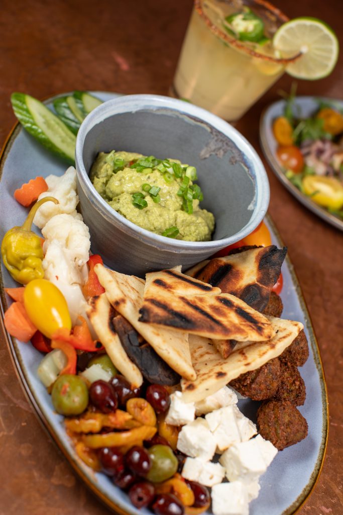 Mezze Platter with crispy falafel, avocado hummus, cucumber, tomatoes, pickled vegetables, spicy olives, feta and grilled naan bread.